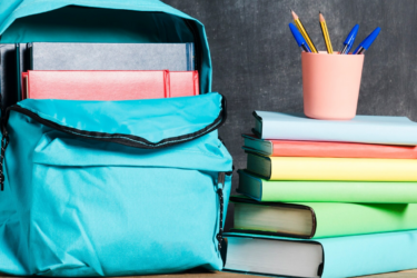 backpack full of books next to a stack of books with a pencil cup of pencils on top