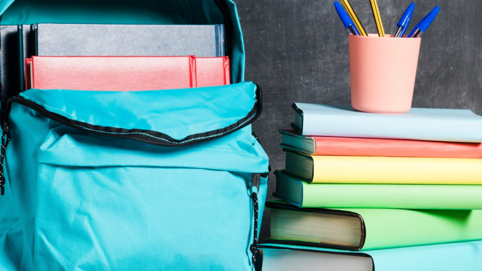 backpack full of books next to a stack of books with a pencil cup of pencils on top