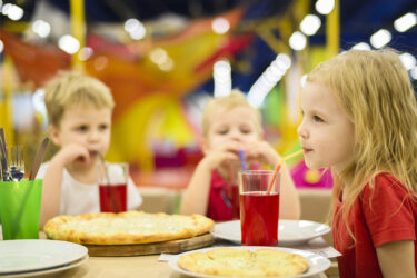 three kids sitting at a table with pizza drinking juice out of cups