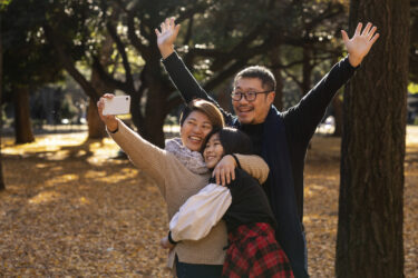 family taking a selfie together in front of a park landscape in the fall