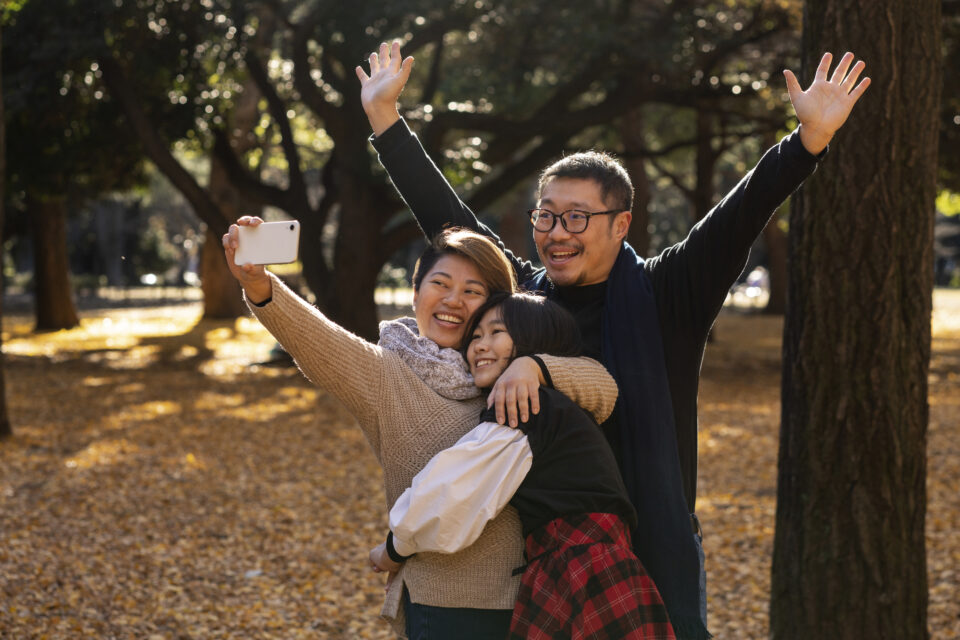 family taking a selfie together in front of a park landscape in the fall