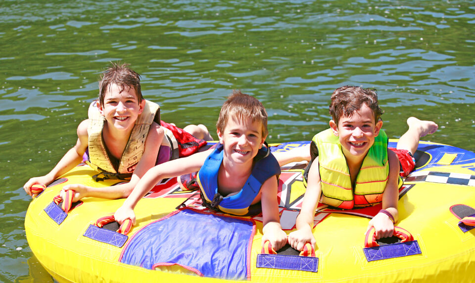 three boys tubing on a lake at sleepaway camp
