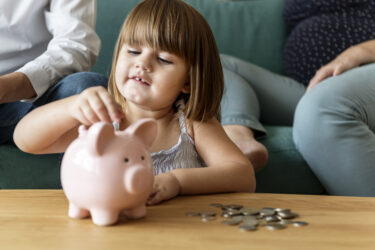 kid saving money, putting coins into a piggy bank