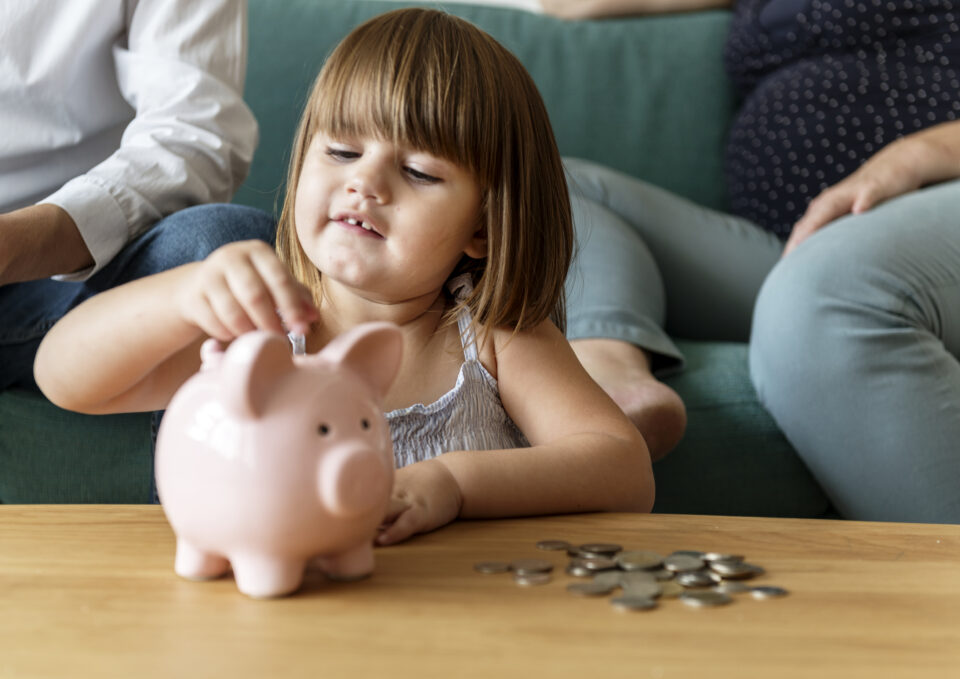 kid saving money, putting coins into a piggy bank