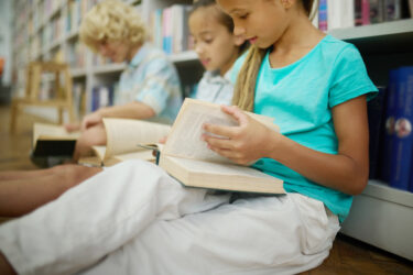 kids reading books on the floor next to the shelves in a library