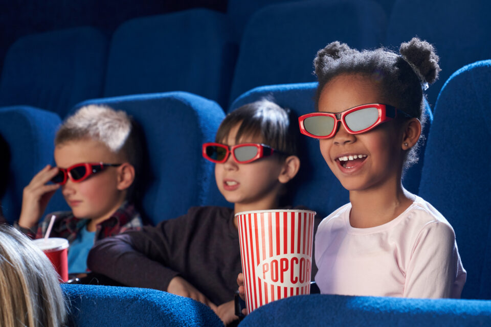children watching a movie in a movie theatre with poporn and 3d glasses